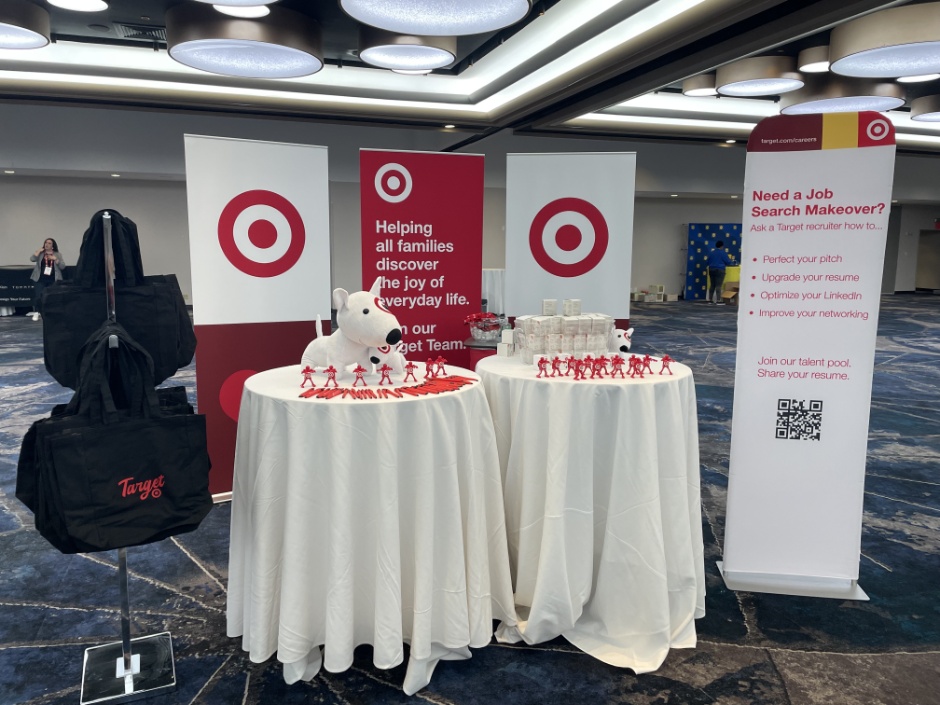A booth at an event with two tables filled with giveaway items and Target branded posters in the background.