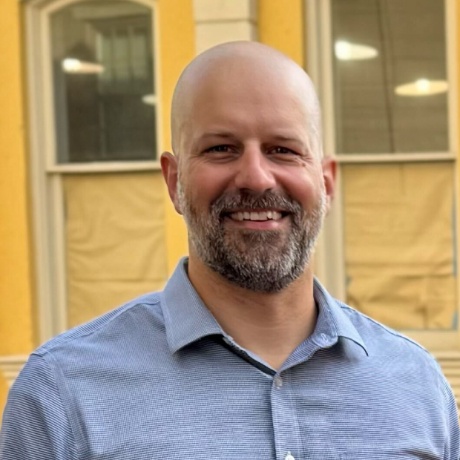 Jake K. smiles warmly outdoors.