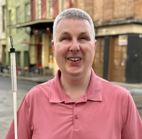 Steve D., smiling outdoors and holding a white cane.