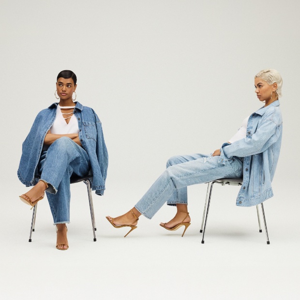 Two models show off denim looks from the collection while reclining in chairs.