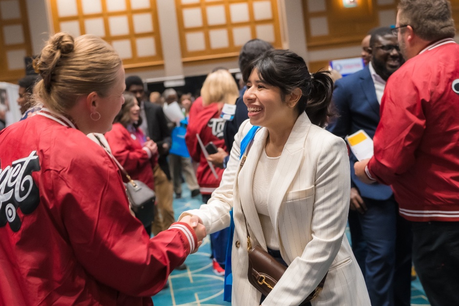 Two people shake hands in a crowded room.