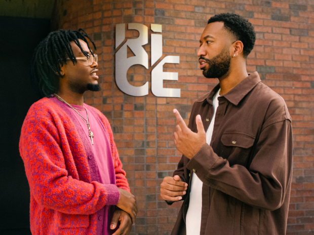 Two men stand in animated conversation in front of a brick wall. Framed between them on the wall is the logo for the Russell Innovation Center for Entrepreneurs.
