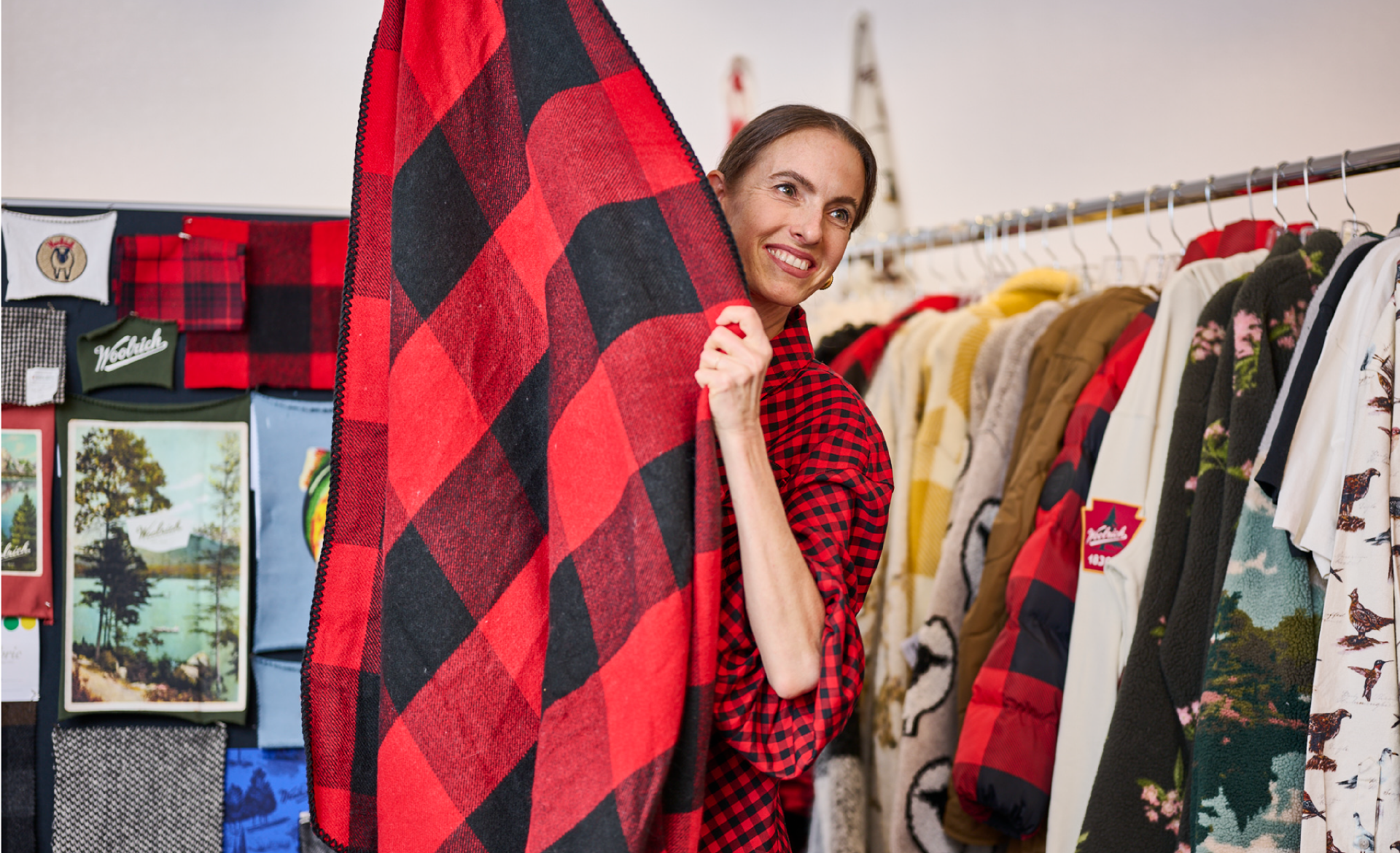 Target’s Gigi Guerra stands in front of a rack of Woolrich x Target clothes and holds up a Woolrich black and red plaid piece of fabric.
